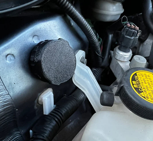 Apple AirTag in a black magnetic holder, stuck to a steel panel and hidden in a car engine bay