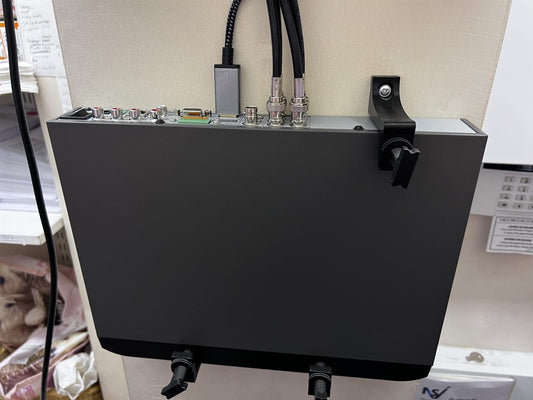 Grey CCTV DVR held on a wall by three separate adjustable brackets, the top bracket screwed to the wall beside the connectors