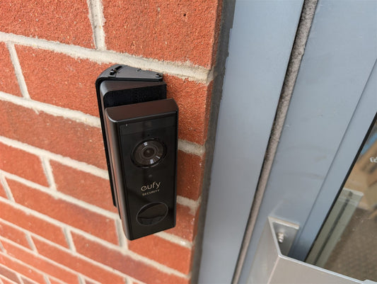 Eufy video doorbell on a black adjustable wedge mount, fixed to a brick wall beside a front door